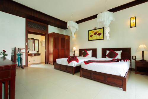 a bedroom with two beds and a woman standing in a room at Hoi An Garden Villas in Hoi An