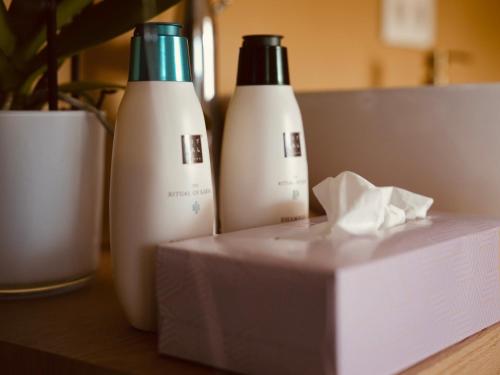 two bottles of shampoo and a box on a table at L'Amarante chambres d'hôtes OU gîte citadin in Theux