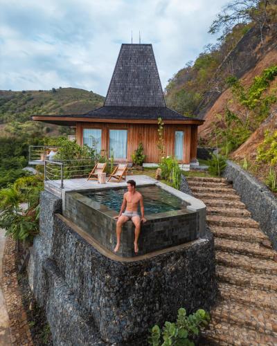 a man sitting in a swimming pool in front of a house at Menjaga Bay in Labuan Bajo