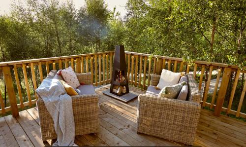 a deck with two wicker chairs and a fireplace at Yurtshire Eavestone Lake - Willow in Ripon