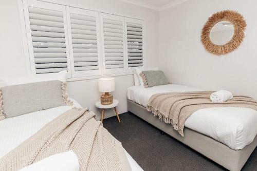 a white bedroom with two beds and a mirror at 'Admirals' Coastal Haven - 200mtrs from Beach in Mooloolaba