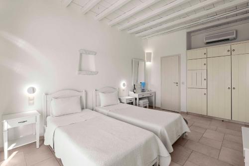 a white bedroom with two beds and a desk at Anthea Hotel in Tinos Town