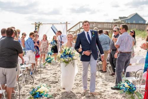 a bride and groom walking down the aisle at a beach at Most Requested 16 Br Oceanfront Home in Holden Beach in Holden Beach