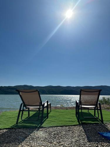 two chairs sitting on the grass by the water at Pensiunea CASA VISELOR in Sviniţa
