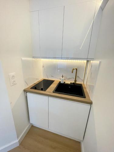 Elle comprend une petite cuisine avec un évier et des placards blancs. dans l'établissement Havre de paix en bord de plage, à Moëlan-sur-Mer