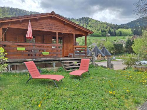 a log cabin with two chairs and an umbrella at Le Repaire de Mitzerlé in Mitzach