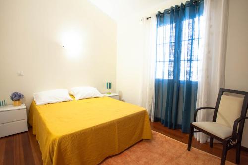 a bedroom with a yellow bed with a chair and a window at Villa Margarida in Ponta do Sol