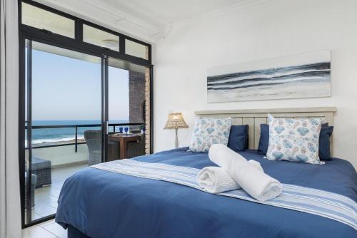 a bedroom with a blue bed with a view of the ocean at Summer Rocks 10 in Uvongo Beach