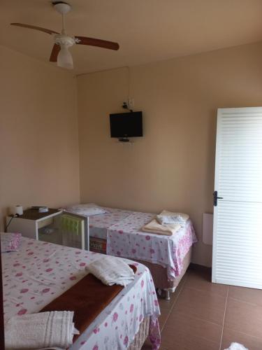 a room with two beds and a tv on the wall at Hospedaria Coração de Pedra in São Thomé das Letras