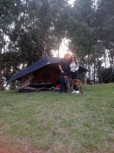 a man and woman standing next to a tent with a dog at Hospedaje Guatavita cabaña tippie in Guatavita