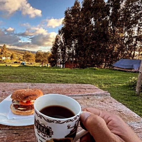 a person holding a cup of coffee and a hamburger at Hospedaje Guatavita cabaña tippie in Guatavita