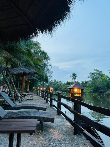 a row of benches and umbrellas next to a river at Bamboo Eco Village in Can Tho