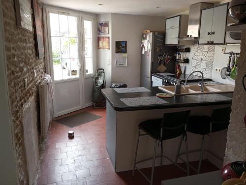 une cuisine avec un évier et un comptoir avec des tabourets dans l'établissement Maison mer plage du débarquement Caen Nord, à Bernières-sur-Mer