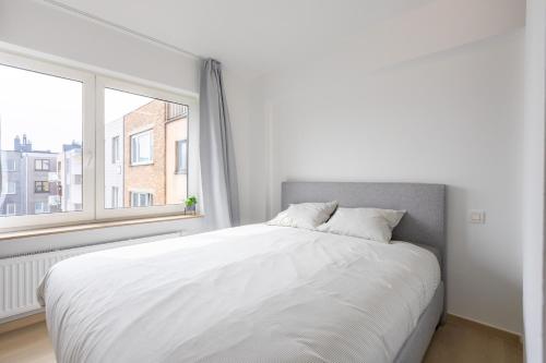 een wit bed in een witte kamer met een raam bij Maison Anna by Exclusive-Stays in Oostende