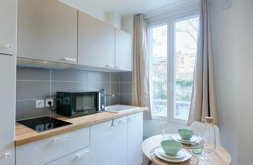 une cuisine avec des armoires blanches, une table et une fenêtre dans l'établissement Appartement Vacances, à Laval