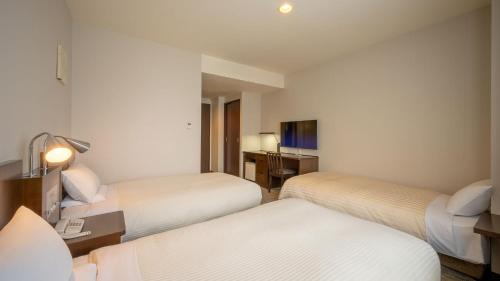 a hotel room with two beds and a desk at JR-East Hotel Mets Fukushima in Fukushima