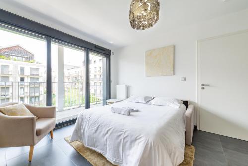 a white bedroom with a bed and a chair at L'Ambre - T2 Lumineux - Parking, RER A, Disneyland in Montévrain