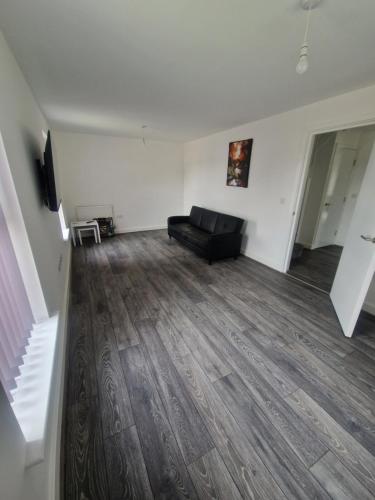 an empty living room with a black couch and wooden floors at Sweet Peace Home in Leeds