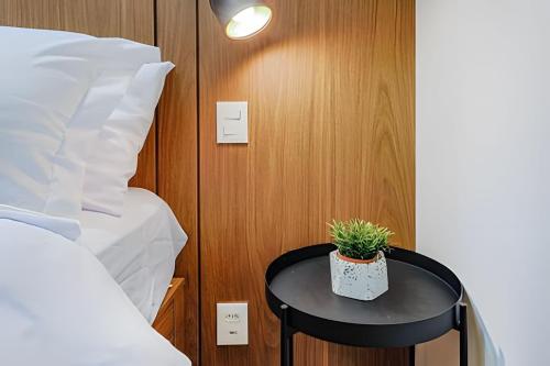 a small table with a plant on it next to a bed at HomeCO - Conforto na esqui praia in Niterói