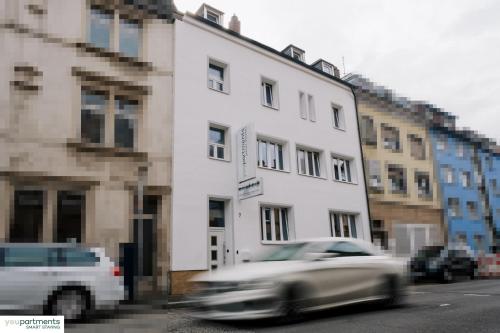 a car driving past a white building on a street at YOUPARTMENTS - zentrale Micro Apartments in Kaiserslautern