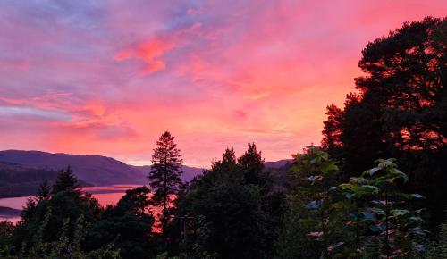 a sunset over a lake with trees in the foreground at Ronaldsay Log Cabin in Strontian