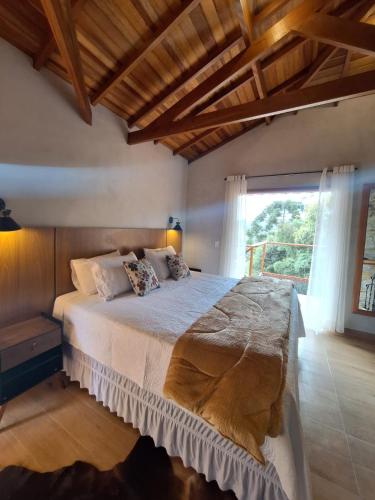 a bedroom with a large bed with a large window at Chalés Cantinho do Céu in Monte Verde