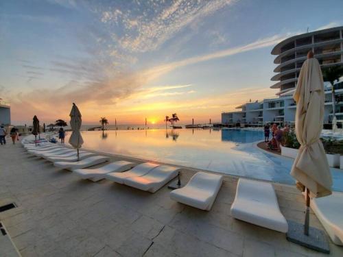 a pool with white lounge chairs and umbrellas at sunset at Beachfront Bliss at Aria Ocean Flamingos in Nuevo Vallarta