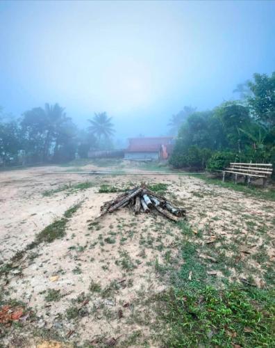 a dirt field with trees and a house in the background at Coorg Stream Side Homestay in Ponnampet