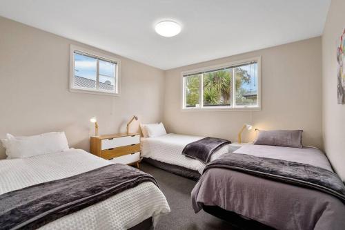 two beds in a room with two windows at Family friendly - 10min drive to Chch city centre in Christchurch