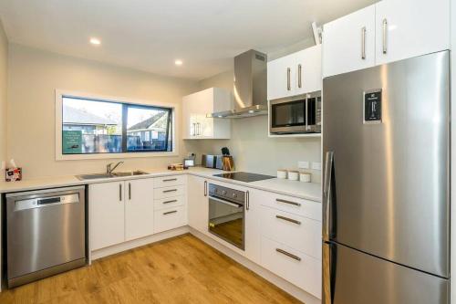 a kitchen with white cabinets and a stainless steel refrigerator at Family friendly - 10min drive to Chch city centre in Christchurch