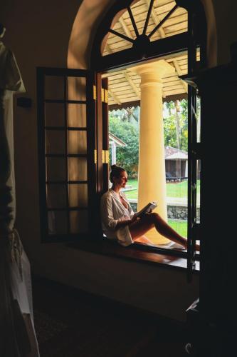 a woman sitting in a window reading a book at Heenatigala Walawwa in Talpe