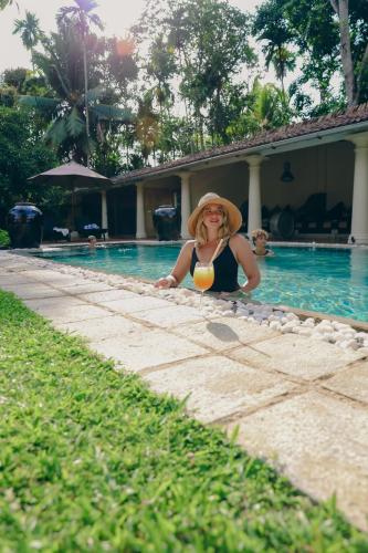 a woman in a hat sitting in a swimming pool at Heenatigala Walawwa in Talpe
