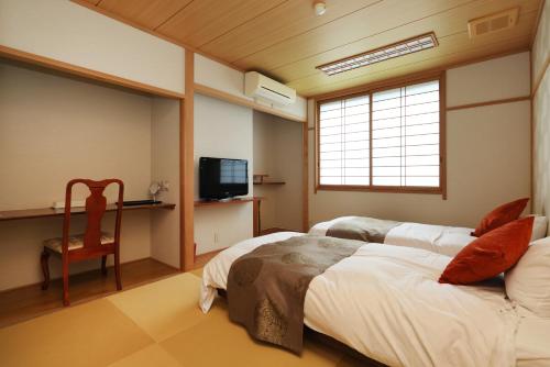 a bedroom with two beds and a tv and a chair at Dogo-no-Yado Katsuragi in Matsuyama