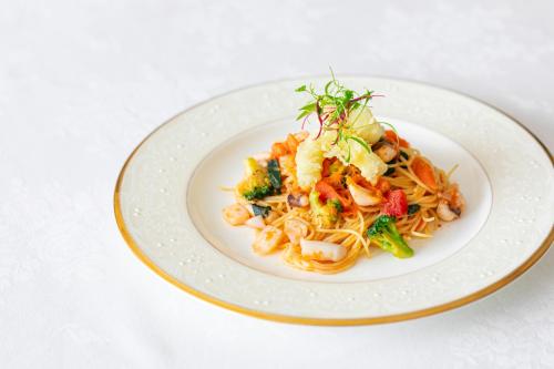 a white plate of pasta with shrimp and vegetables at GrandEmpireHotel in Onojo