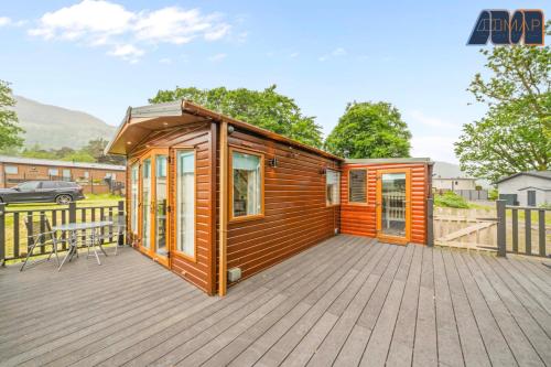 a wooden cabin on a deck with a table at Loch Lomond - Ard Lui Lodge in Ardlui