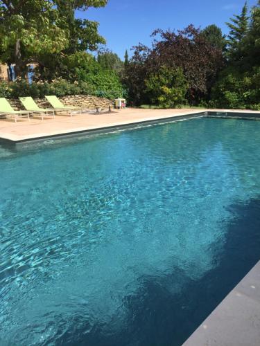 une piscine d'eau bleue avec des chaises et des arbres dans l'établissement La maison Danna, à Lauris