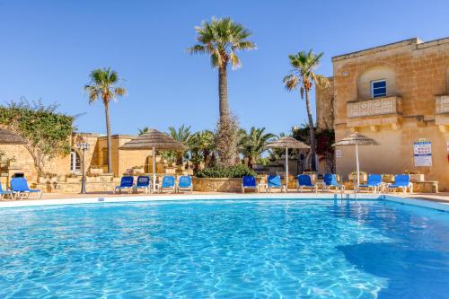 a large swimming pool with blue chairs and palm trees at Villagg tal-Fanal in Għasri