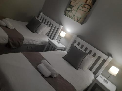 two beds in a small bedroom with two lamps at Oakwood Lodge in Bloemfontein