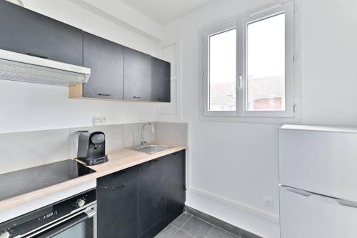 d'une cuisine avec des placards noirs, un évier et une fenêtre. dans l'établissement Studio Sympathique proche de Paris - Montreuil, à Montreuil