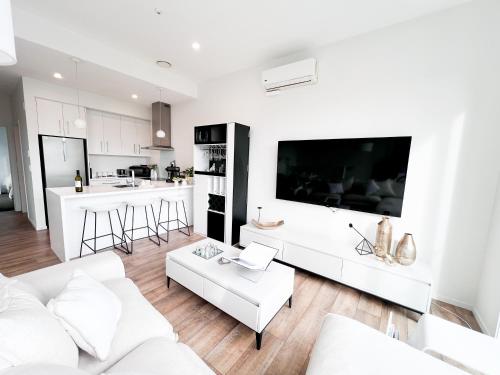 a living room with white furniture and a large screen tv at Luxury 2 Bedroom Apartment with cocktail bar and espresso machine in Auckland