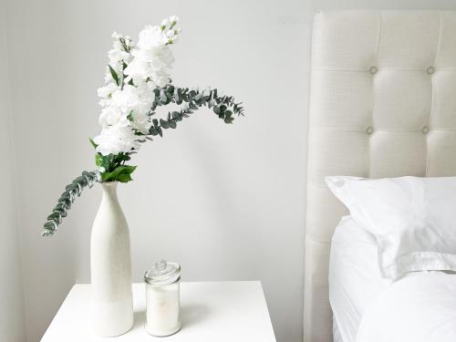 a white vase with flowers on a table next to a bed at Luxury 2 Bedroom Apartment with cocktail bar and espresso machine in Auckland