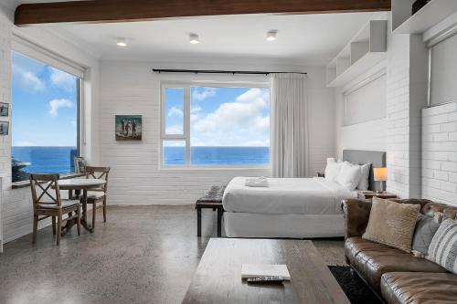 Un dormitorio con una cama, una mesa y un sofá. en Upscale Cliffside Studio with Ocean Views North Bondi, en Sídney