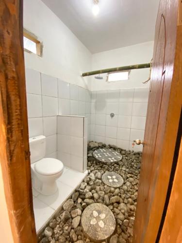 a bathroom with a toilet and rocks on the floor at Opik Homestay Tete Batu in Tetebatu
