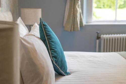 a bed with blue and white pillows and a window at Woodland Manor Hotel in Bedford