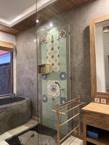a bathroom with a glass shower with a tub at Abitama Villa in Ubud