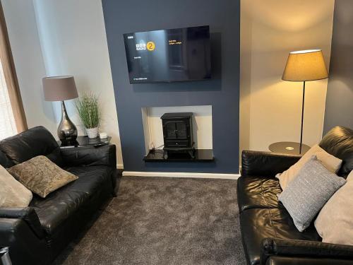 a living room with two black leather couches and a fireplace at Modernised 4bed stay-away-home in Runcorn sleeps 7 in Runcorn