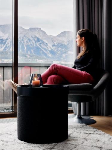 a woman sitting in a chair looking out a window at ARX Guesthouse in Schladming