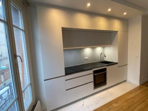 une cuisine avec des armoires blanches, un évier et une fenêtre dans l'établissement Beautiful contemporary and cosy flat in Paris, à Boulogne-Billancourt