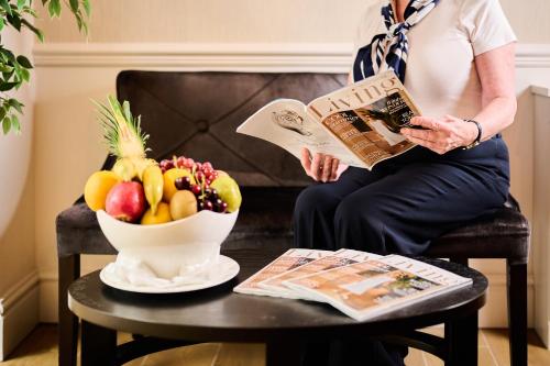 a woman sitting in a chair reading a newspaper next to a bowl of fruit at Milford Hall Salisbury in Salisbury