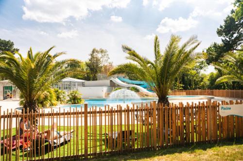 une clôture en face d'une piscine bordée de palmiers dans l'établissement Camping Officiel Siblu Bois de Bayadène, à Piriac-sur-Mer